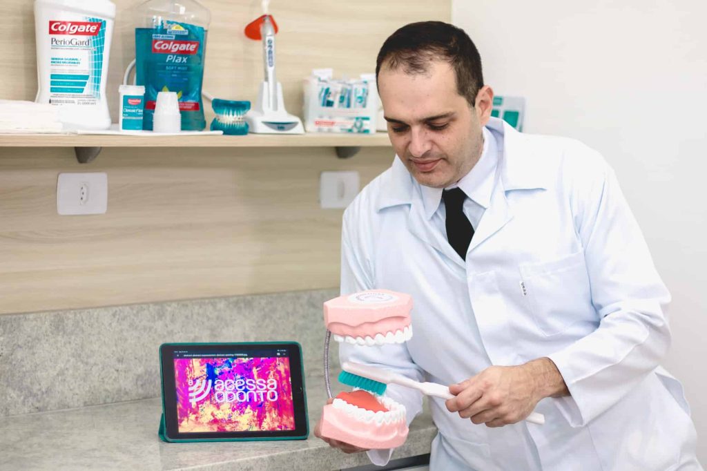 Prof. Dr. Rafael Muglia realizando orientação de higiene bucal com modelo didático para prevenção de doenças gengivais.