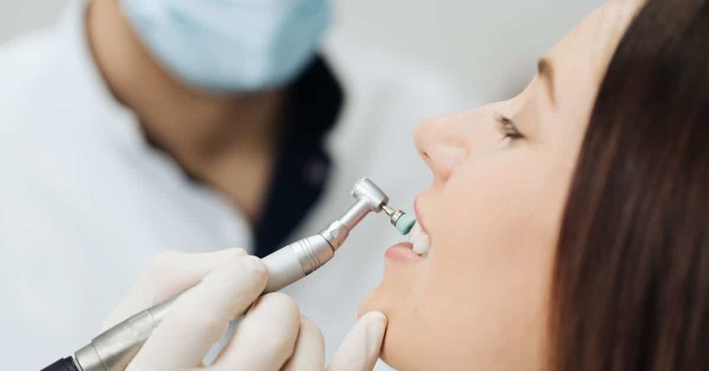 Dentista realizando profilaxia profissional com escova rotatória para prevenção de tártaro e doenças gengivais na Clínica Muglia.