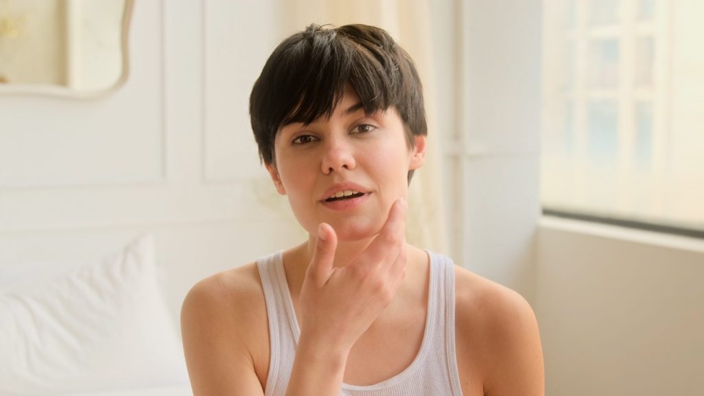 Paciente apontando para a região do mento (queixo) após procedimento de preenchimento facial.