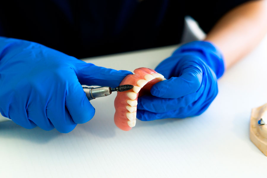 Dentista realizando o ajuste fino e polimento de uma prótese total (dentadura) para garantir o conforto e a estética da reabilitação oral.